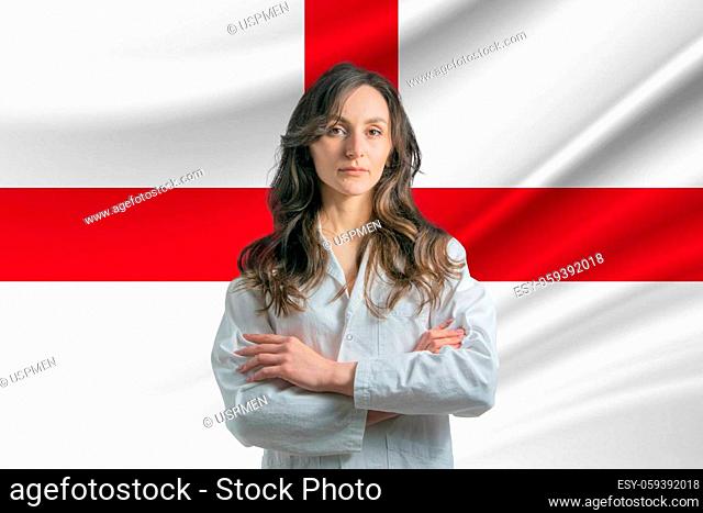 Medicine in England. Happy beautiful female doctor in medical coat standing with crossed arms against the background of the flag of England