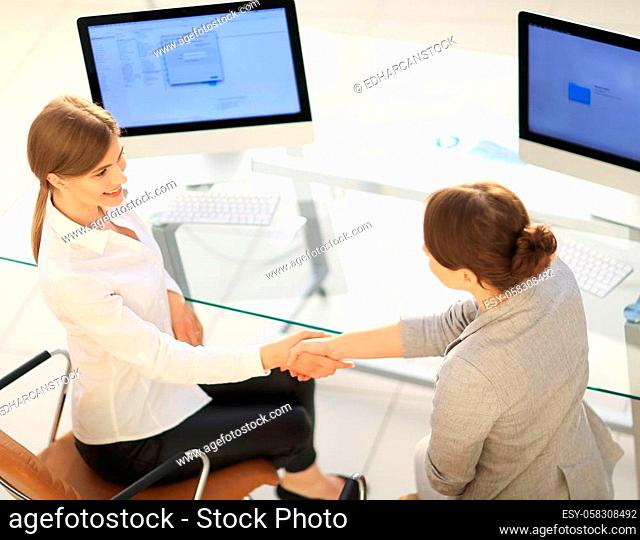 business woman shakes hands with the officer sitting near the desktop. business concept