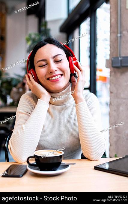 Happy woman with eyes closed listening music through wireless headphones at cafe