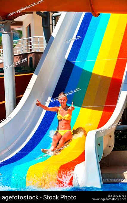 Child on water slide at aquapark show thumb up. Child slides with flowing water in aqua park. Summer child water park holiday. Outdoor