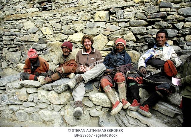 Four friendly man in traditional dress made of wool and a Western mountaineer sit at a wall Phu Nar-Phu Annapurna Region Nepal