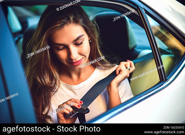 Beautiful woman with phone smiling while sitting on the back seat in the car