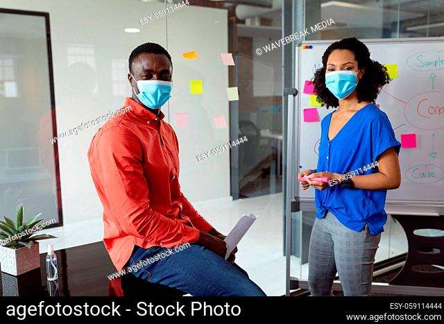 Portrait of diverse male and female colleague in face masks brainstorming in office