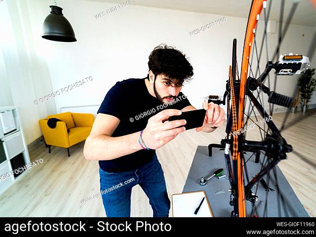 Man photographing bicycle parts through smart phone at home