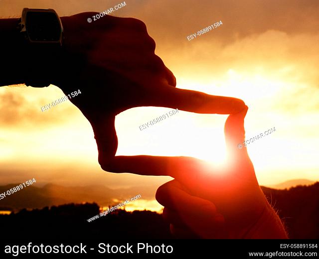 Close up of hands with watch making frame gesture. Dark misty valley bellow in landscape. Sunny autumn daybreak in mountains