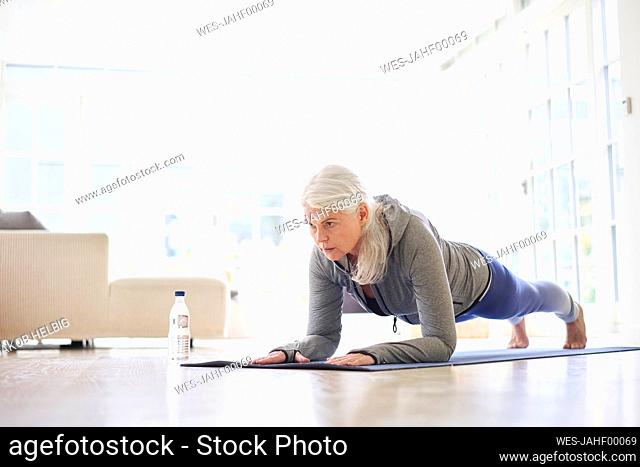 Retired active senior woman practicing plank position on mat at home