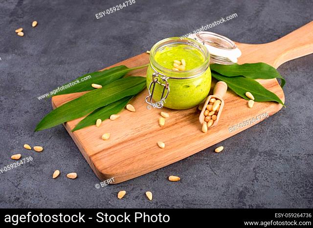 Pesto made from wild garlic, pine nuts and feta cheese in a glass, with fresh leaves on a dark textured background, empty space for text