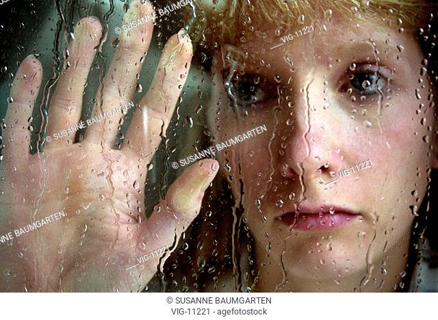 Symbolic photo to the topics: depression, sadness, loneliness, etc. Face of a young, sad woman behind a wet windowpane. - BONN, GERMANY, 20/02/2002