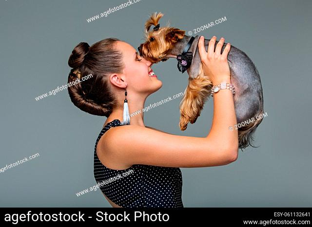 Beautiful young teenage girl in dress holding small cute yorkshire terrier dog. Copy space. Studio shot on grey background