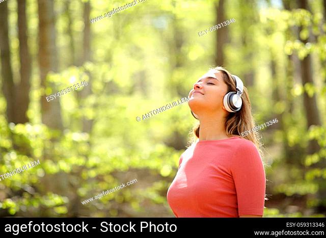 Woman meditating wearing headphones listening audio guide in a forest