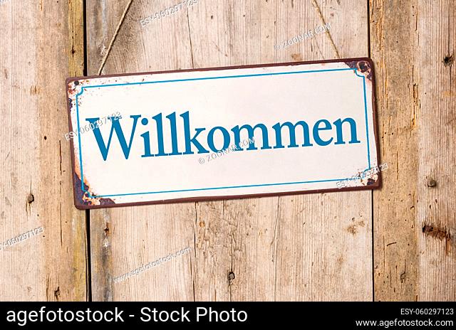 Old metal sign in front of a rustic wooden wall - Welcome - Willkommen German