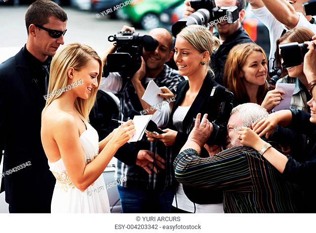 A stunning young actress signing autographs on the red carpet while swamped by paparazzi