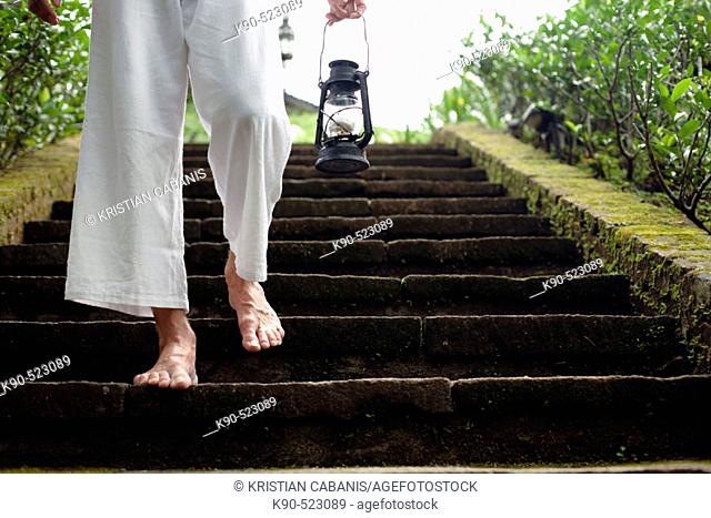 Man walking down the earthern stairs carrying an oil lamp at Losari Coffee Plantation in West Java, Indonesia, South East Asia