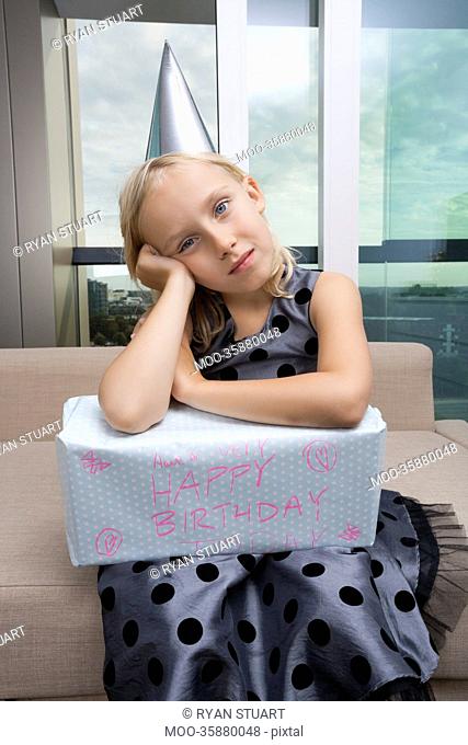 Portrait of sad girl with birthday gift sitting on sofa at home