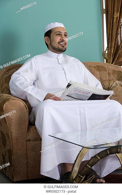 Arab man sitting in a sofa holding a newspaper