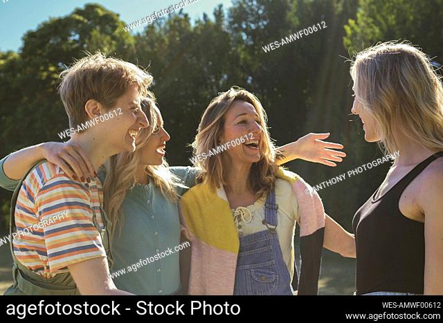 Cheerful friends greeting each other at park on sunny day