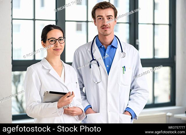 Portrait of two dedicated doctors smiling and looking at camera while holding a tablet and a folder with medical records