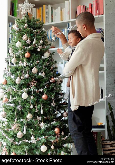 Father and baby daughter decorating Christmas tree in living room