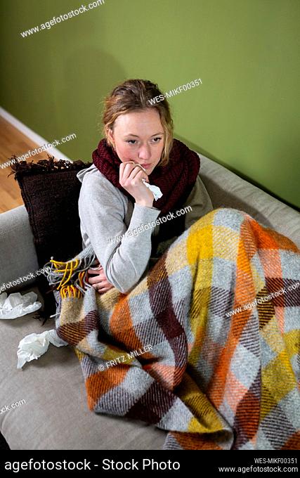 Sick young woman wrapped in blanket relaxing on couch
