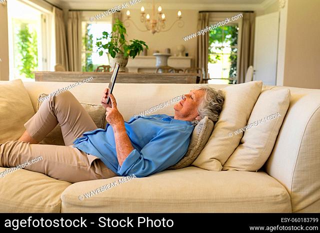 Senior caucasian woman lying on sofa using tablet