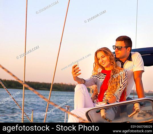 Beautiful couple taking a selfie on a sailing boat at summer sunset
