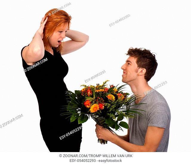 Young man offers his surprised girlfriend a large bouquet of flowers, isolated on a white background