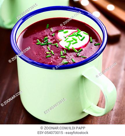 Fresh homemade beetroot cream soup in enamel cup, garnished with cream and chives (Selective Focus, Focus one third into the soup)