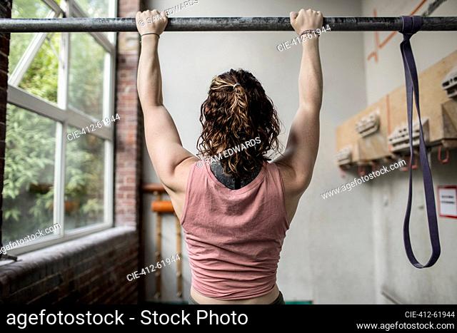 Muscular young woman working out at bar in gym