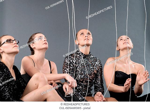 Young women looking at hanging strings, grey background
