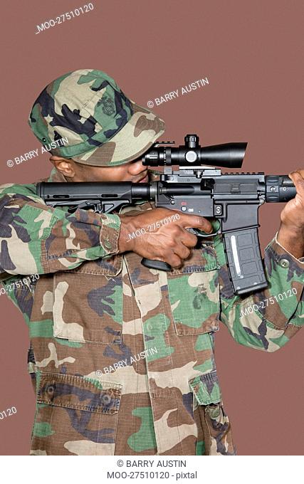 Male US Marine Corps soldier aiming M4 assault rifle over brown background