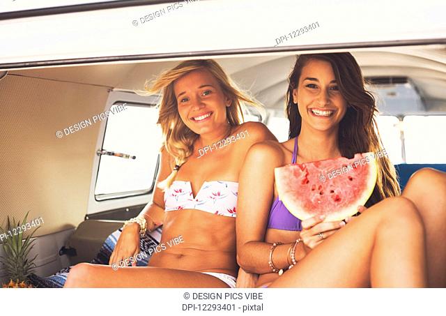 Surfer Girls Beach Lifestyle, Friends Hanging Out Eating Watermelon In The Back Of Classic Vintage Surf Van On The Beach At Sunset