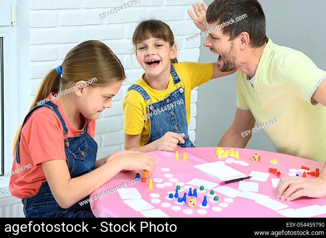 The girl and dad are screaming and laughing cheerfully, the other girl is considering the next move in the board game