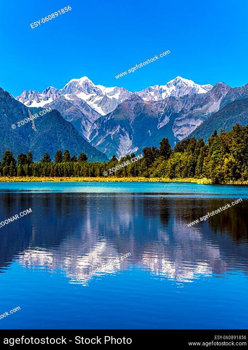 The forests and Mount Cook and Mount Tasman. Magnificent snow-capped mountains surround the smooth, cold waters of Lake Matheson