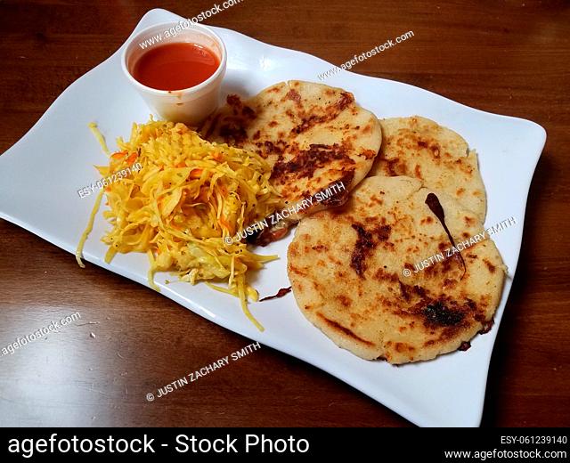 pupusa or fried tortilla stuffed with cheese on plate with cabbage and tomato sauce