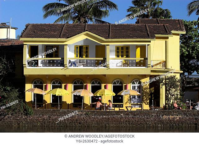 Attractive pastel yellow Riverside Hotel with sunshades on outside terrace Baga Goa India
