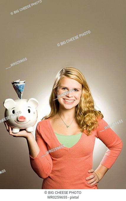 Teenage girl holding piggy bank with money