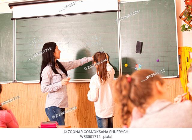 Woman teacher helping pupil to solve math example at the blackboard