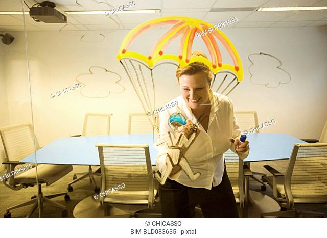 Caucasian businesswoman drawing a golden parachute on conference room wall