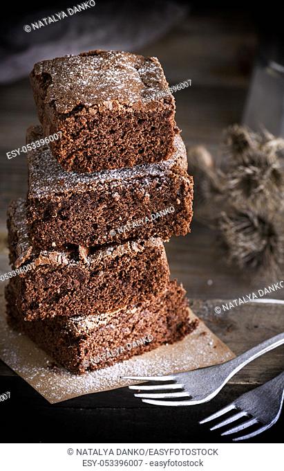 stack of square pieces of chocolate cake baked brownies and two iron forks, close up