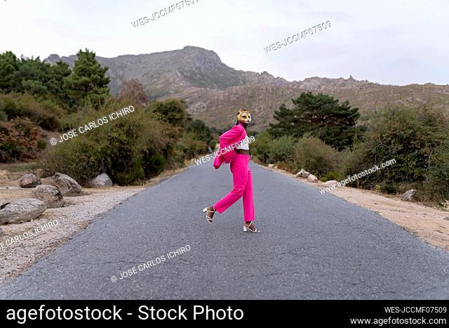 Woman wearing tiger mask standing on road in front of mountain