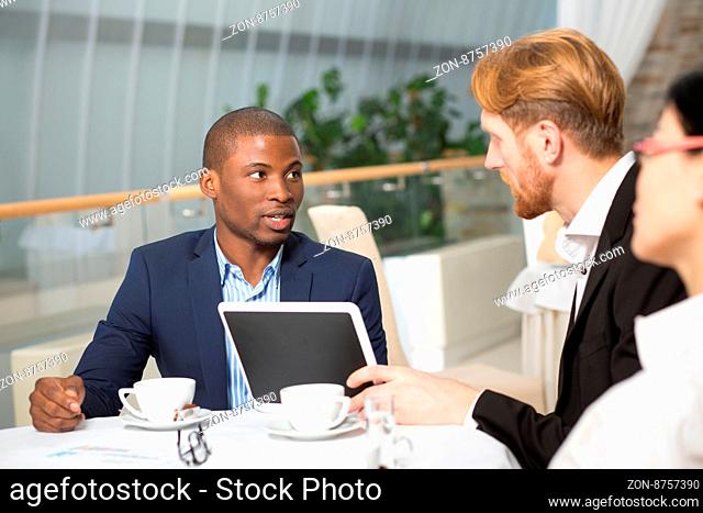 Communication betweent business people during business meeting in restaurant. People sitting at table and looking at tablet PC