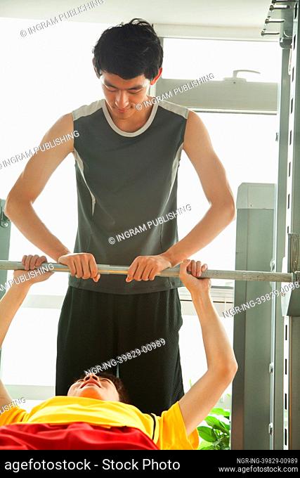 Young men weight lifting with his personal trainer in the gym