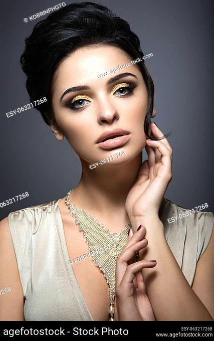 Beautiful brunette woman with perfect skin, gold makeup and handmade jewelry. Beauty face. Picture taken in the studio on a grey background