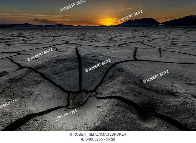 Cracked, dried out soil with small water area and Allgäu Alps in the background at sunrise, Forggensee, Füssen, Ostallgäu, Bavaria, Germany