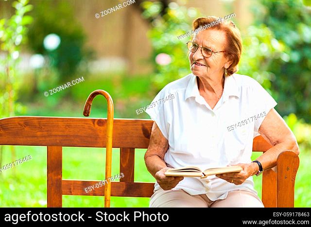 Elderly woman sitting and relaxing on a bench outdoors in park
