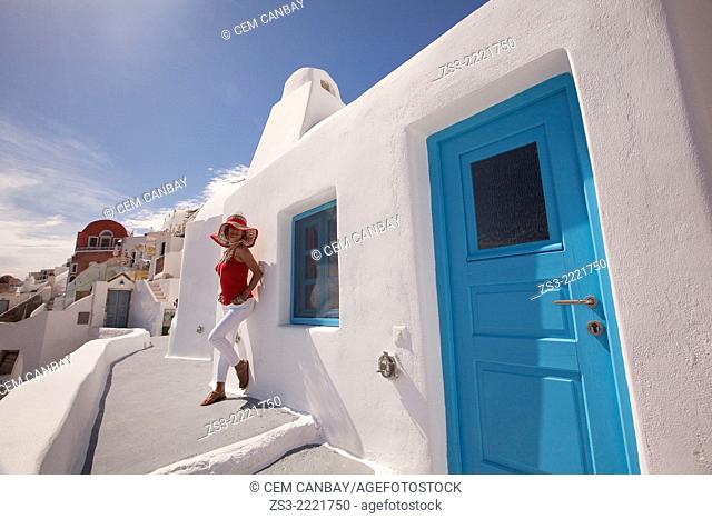 Woman posing in front of a Cyclades house in Oia town, Santorini, Cyclades Islands, Greek Islands, Greece, Europe
