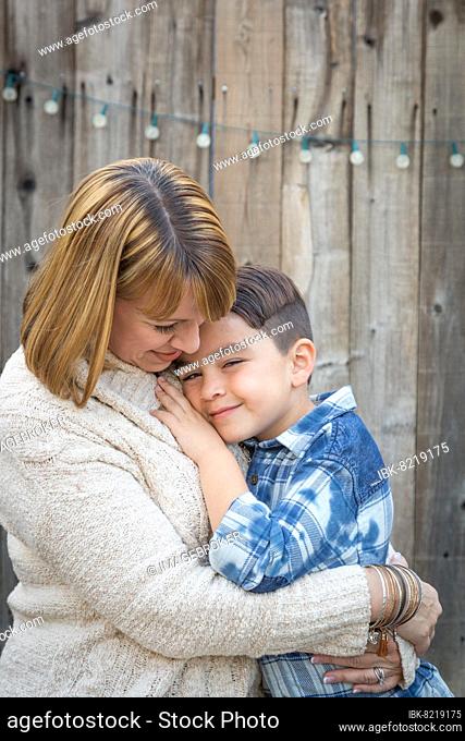Loving mother and mixed-race son hug near fence