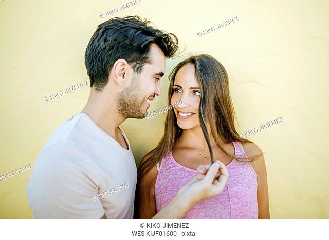 Young couple looking at each other in love against yellow wall