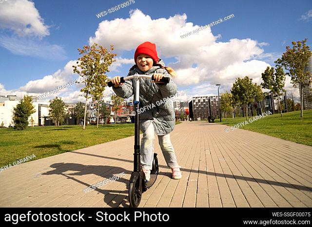 Girl riding toy scooter on footpath at park during sunny day