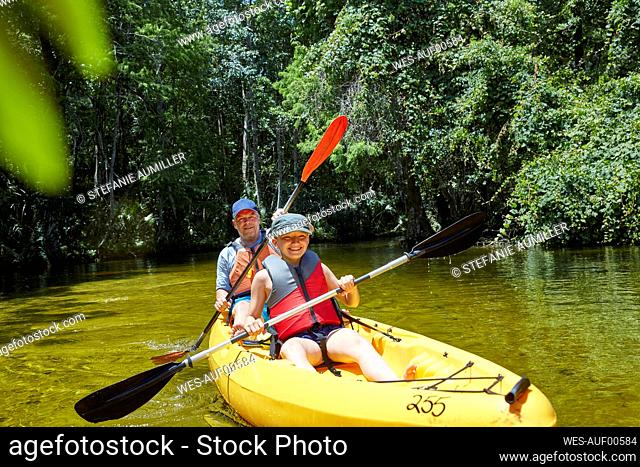 Cheerful daughter kayaking with oar while sitting against father in canoe